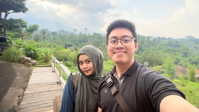 Berdua di jembatan kayu berlatar hutan hijau